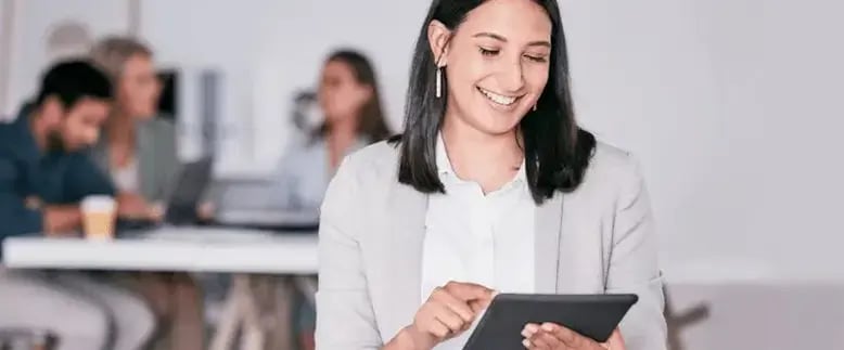 Smiling businesswoman looks at her tablet while her coworkers brainstorm in the background