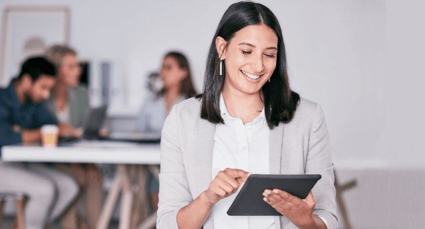 Smiling businesswoman looks at her tablet while her coworkers brainstorm in the background