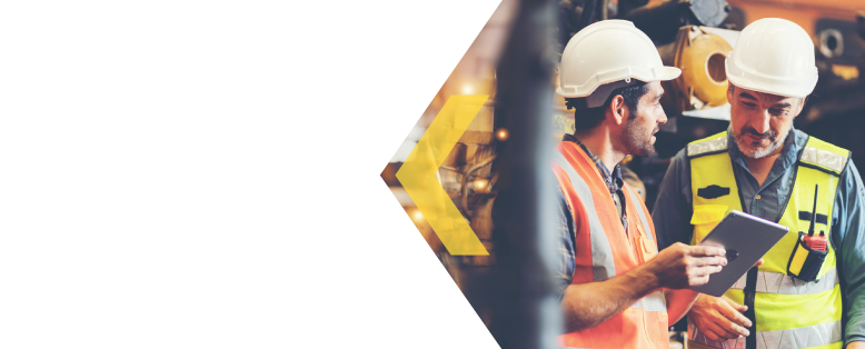 Two warehouse employees in hard hats use a tablet to discuss data from their cloud ERP solution for manufacturing