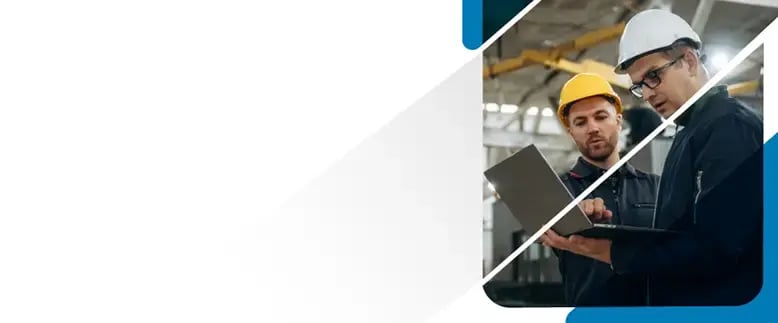 Two men in hard hats look at a laptop while standing in a warehouse